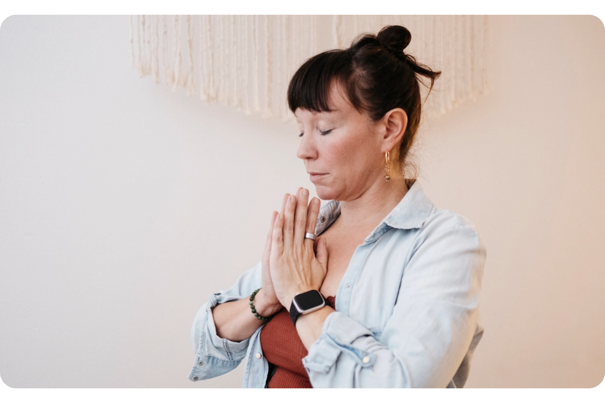 Mezzo busto di Claudia con le mani in Namaskar mudra davanti al petto con gli occhi chiusi i capelli legati e con indosso una camicia di jeans chiara.